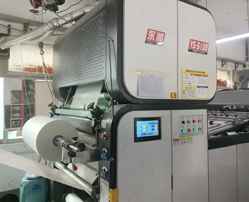 Industrial lamination machine applying protective film to paper.