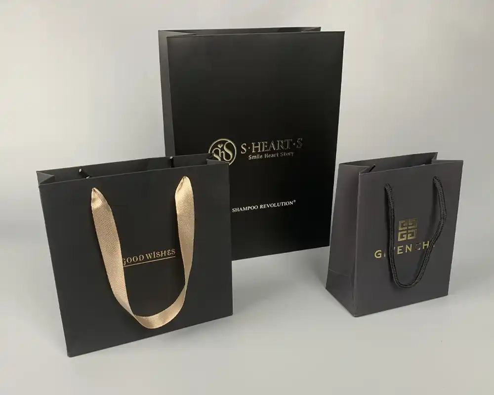 Luxury black custom paper bags with gold foil logos and ribbon handles.