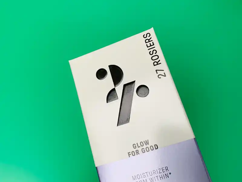 Cosmetic paper box with glossy varnish logo on white and lavender surface