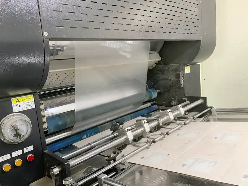 Close-up of lamination machine applying protective film to printed paper sheets